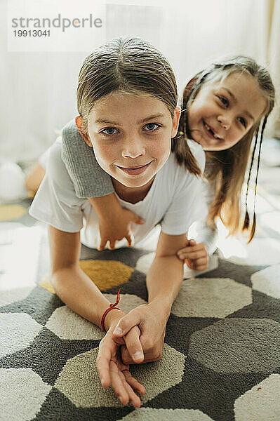 Smiling sisters having fun on carpet at home