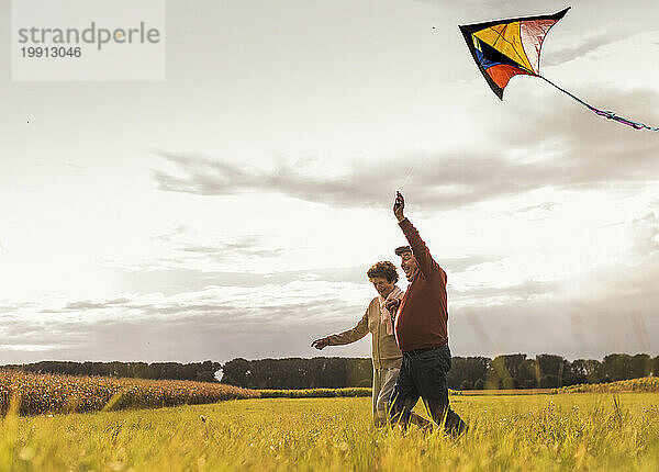 Glückliches älteres Paar  das an einem sonnigen Tag im Feld läuft und Drachen steigen lässt