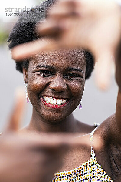 Lächelnde junge Frau gestikuliert mit dem Fingerrahmen