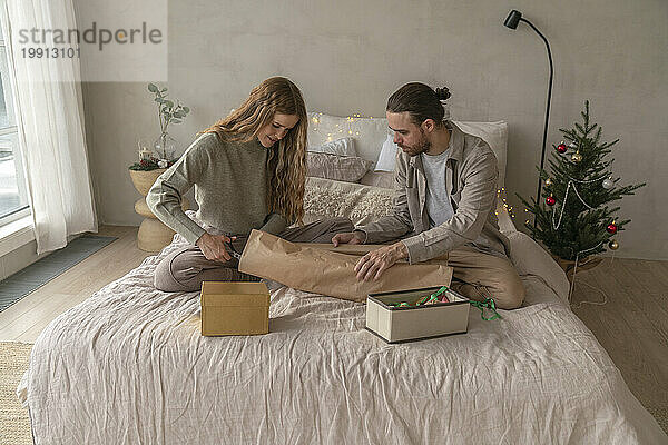 Paar schneidet Geschenkpapier auf dem Bett zu Hause