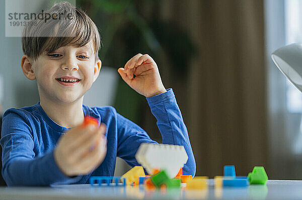 Smiling boy playing with toy blocks at home