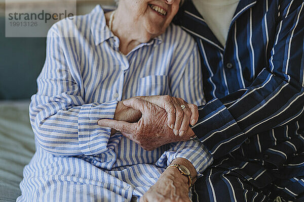 Happy senior woman holding hands with man sitting on bed at home