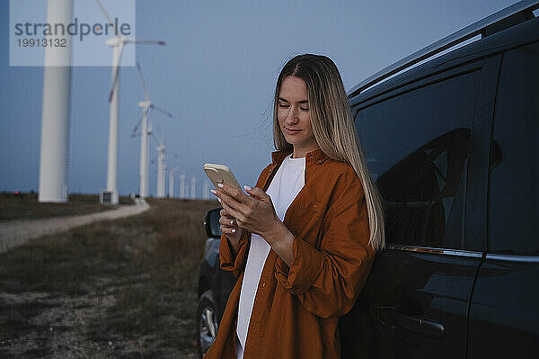 Frau benutzt Smartphone in der Nähe von Auto auf Windkraftanlage