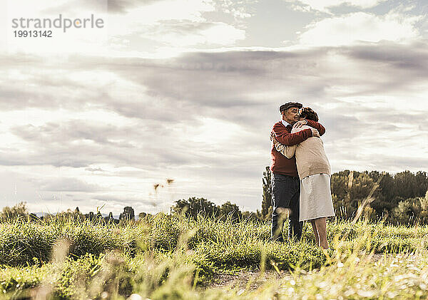 Loving senior couple hugging in field on sunny day