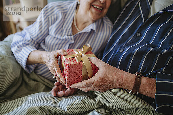 Älterer Mann schenkt lächelnder Frau zu Hause ein Geschenk