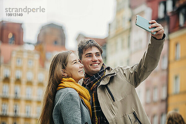 Glücklicher Mann  der auf der Straße ein Selfie mit seiner Freundin per Smartphone macht