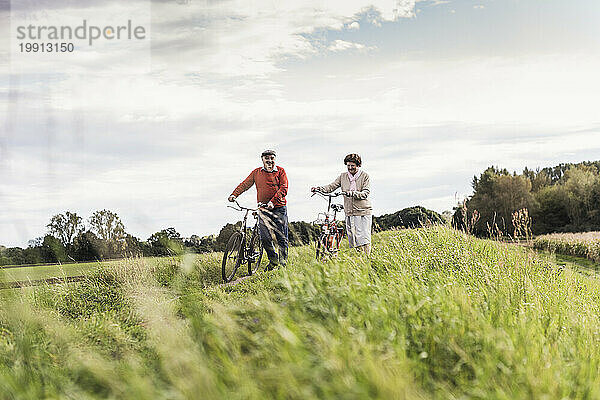 Senior couple walking with bicycles at field