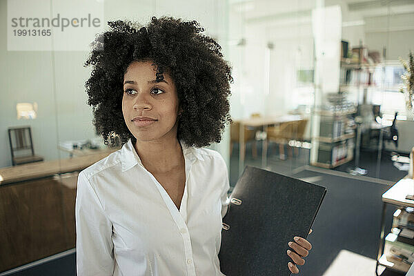 Thoughtful businesswoman holding folder at office