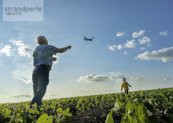 Senior man flying toy airplane with grandson running in field