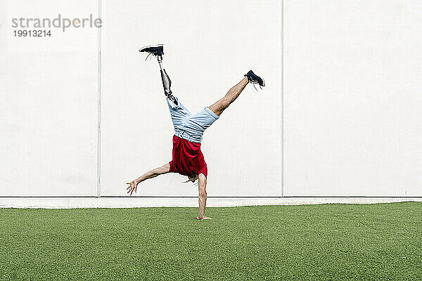 Junger Mann mit Beinprothese macht Handstand vor der Wand