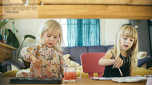 Mädchen malen mit Pinseln und Wasserfarben am Tisch zu Hause