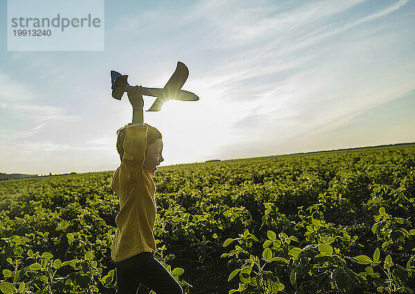 Fröhlicher Junge läuft mit Spielzeugflugzeug auf landwirtschaftlichem Feld unter Himmel