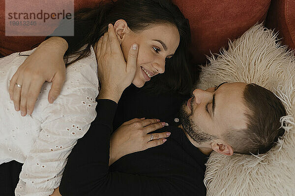 Young man lying down and embracing woman at home