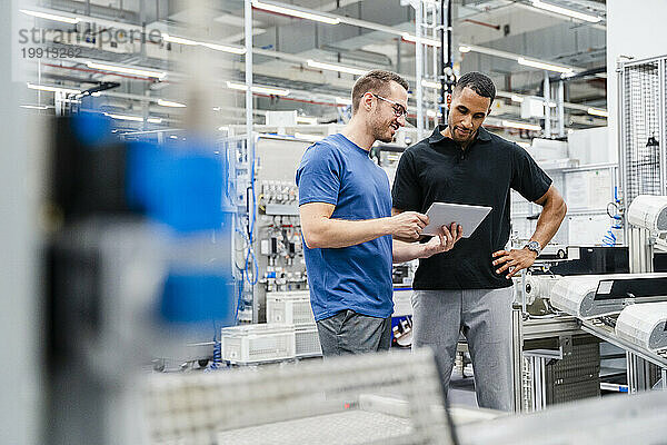 Zwei Kollegen teilen sich in einer Fabrik ein digitales Tablet