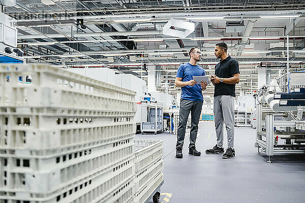 Zwei Kollegen mit digitalem Tablet unterhalten sich in einer Fabrik