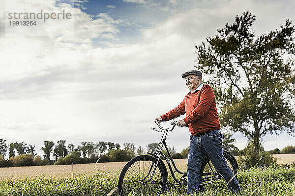Lächelnder älterer Mann  der mit dem Fahrrad im Feld spaziert
