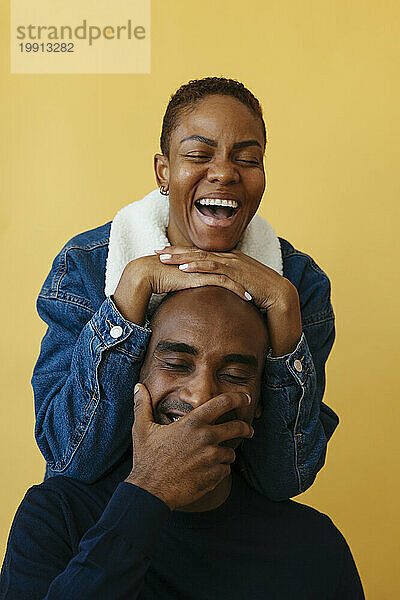 Playful couple laughing against yellow background