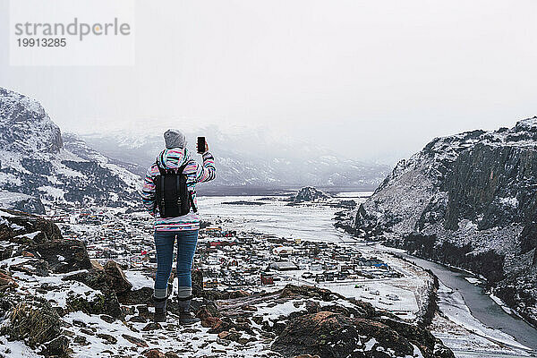 Frau fotografiert schneebedeckte Berge mit Smartphone