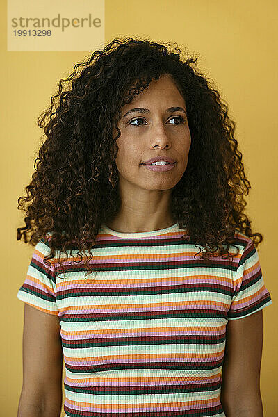 Thoughtful woman wearing striped t-shirt against yellow background