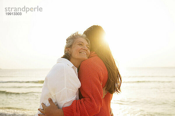 Liebevolle Mutter umarmt Tochter am Strand