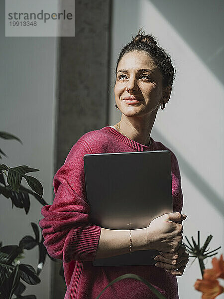 Lächelnde Geschäftsfrau hält Laptop in der Nähe der Fabrik im Büro