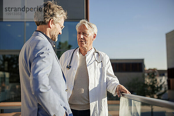 Arzt spricht an sonnigem Tag mit Mann in der Nähe des Geländers