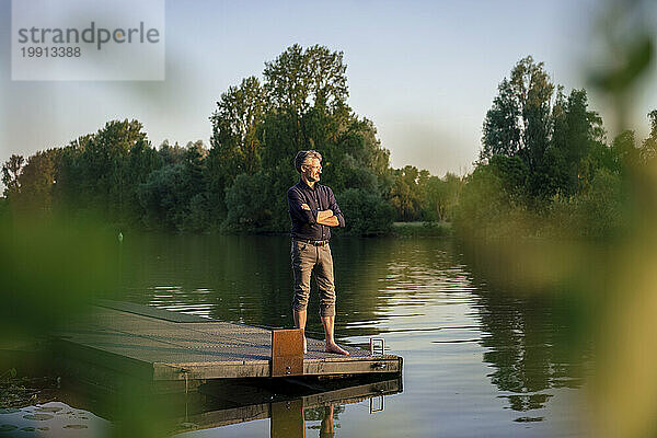 Smiling man with arms crossed standing on jetty near lake