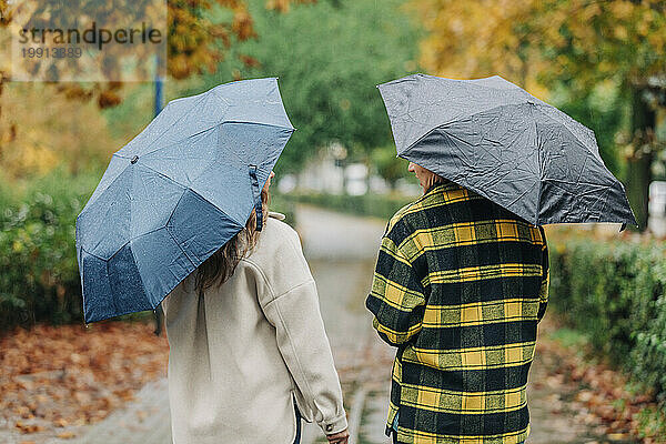 Mutter und Tochter halten Regenschirme in der Hand und gehen im Herbstpark spazieren