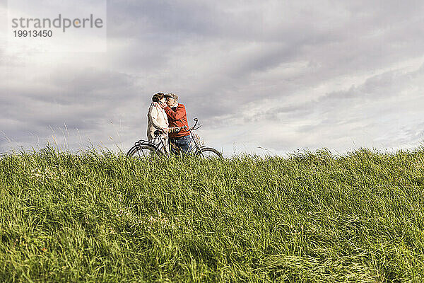 Loving senior couple kissing at field under cloudy sky