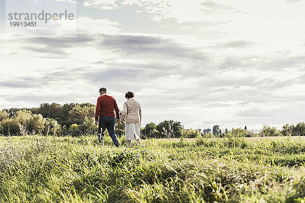 Älteres Paar spaziert unter bewölktem Himmel auf dem Feld