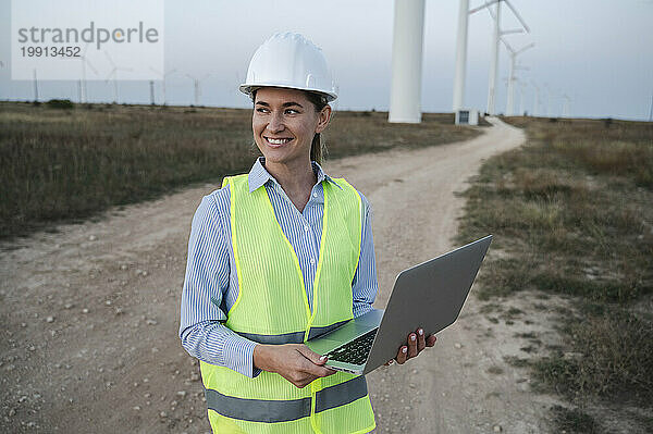 Glücklicher Ingenieur steht mit Laptop am Windkraftfeld