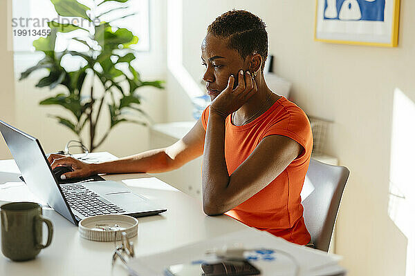 Geschäftsfrau mit der Hand am Kinn nutzt Laptop und arbeitet aus der Ferne im modernen Heimbüro