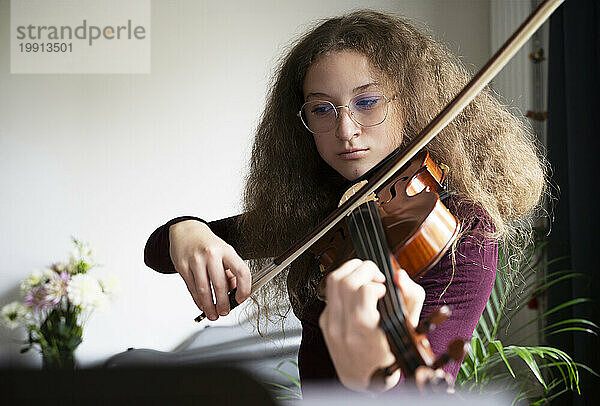 Mädchen mit krausem Haar spielt zu Hause Geige