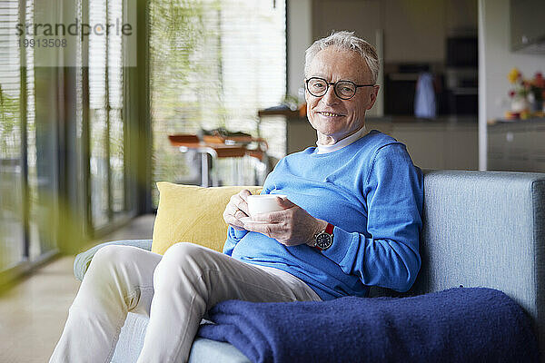Älterer Mann sitzt zu Hause auf der Couch und trinkt eine Tasse Kaffee