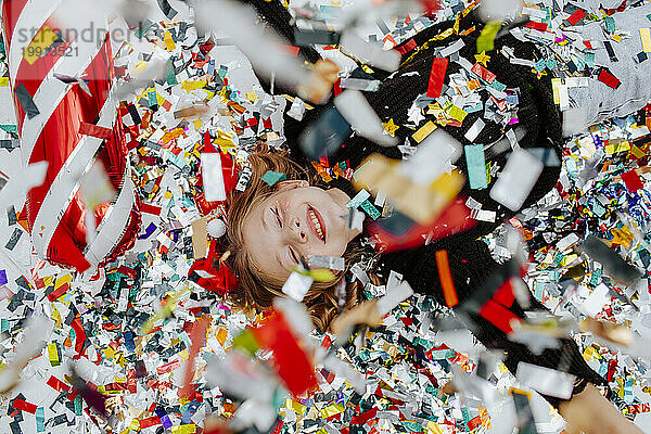 Cheerful girl lying under falling confetti on floor