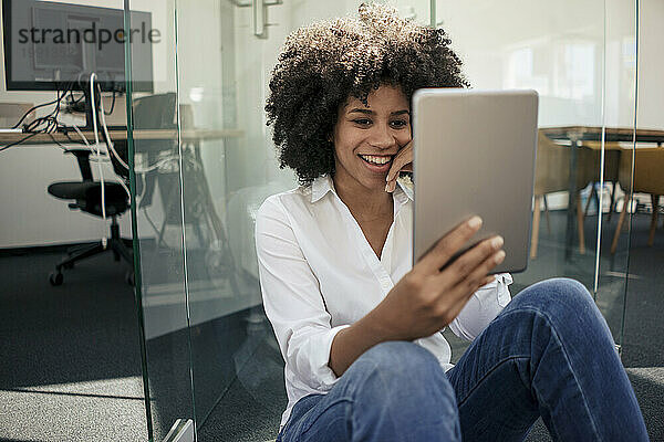 Smiling businesswoman doing video call on tablet PC sitting at office