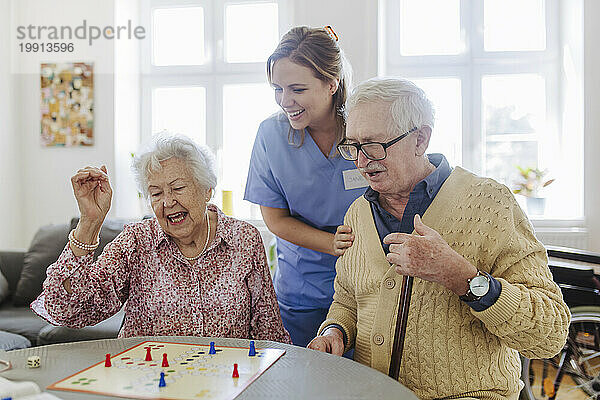 Glückliches älteres Paar spielt Ludo-Spiel mit einem zu Hause stehenden Gesundheitspersonal