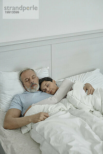 Frau kuschelt ihren Mann  während sie zusammen im Bett schläft