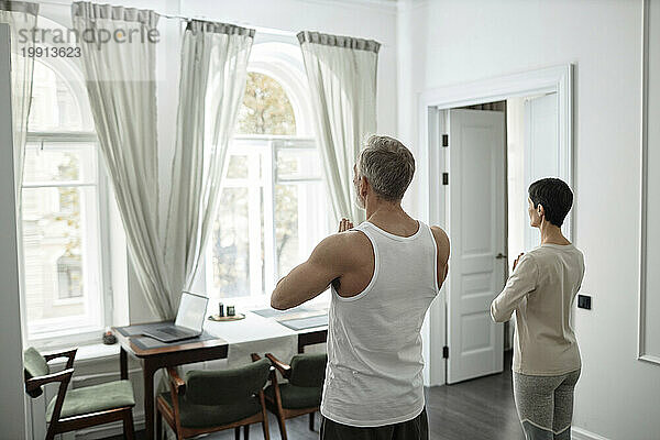 Rückansicht eines erwachsenen Paares  das während der Morgenmeditation zu Hause die Handflächen vor sich faltet