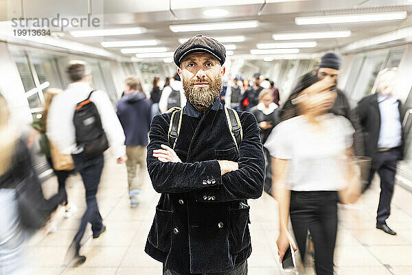 Man with arms crossed standing amidst people moving at subway station