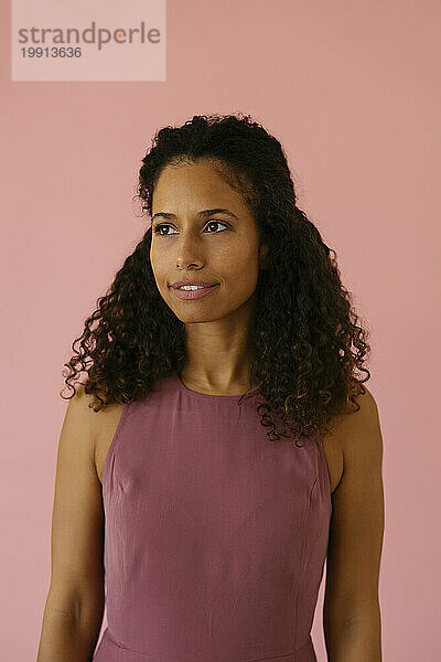 Woman with curly hair standing against pink background