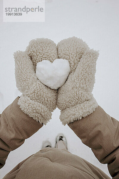 Frau trägt Handschuhe und steht im Winter vor herzförmigem Schnee