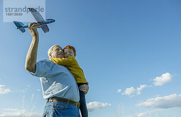 Grandfather and grandson playing with toy airplane under sky