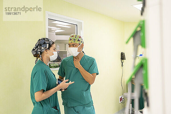 Doctor holding smart phone having discussion with colleague in operating room