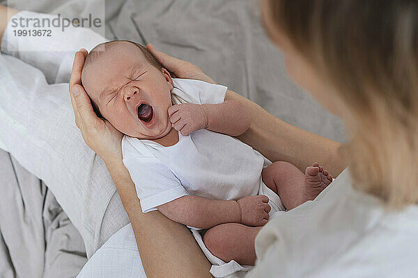 Newborn baby boy sleeping and yawning on mother's lap