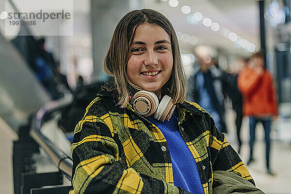 Lächelndes Teenager-Mädchen mit kabellosen Kopfhörern im Einkaufszentrum