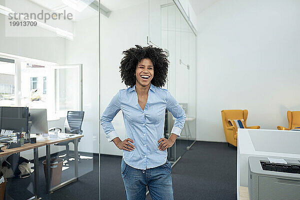 Happy businesswoman standing with arms akimbo and laughing at office