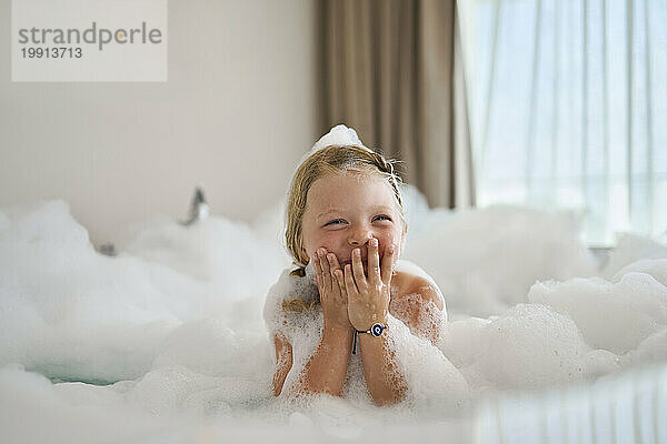 Blondes Mädchen bedeckt den Mund und lacht in der Badewanne