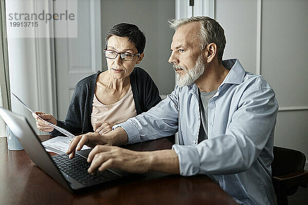 Älteres Paar spricht über Familienunternehmensthemen  während es zu Hause am Tisch vor dem Laptop sitzt