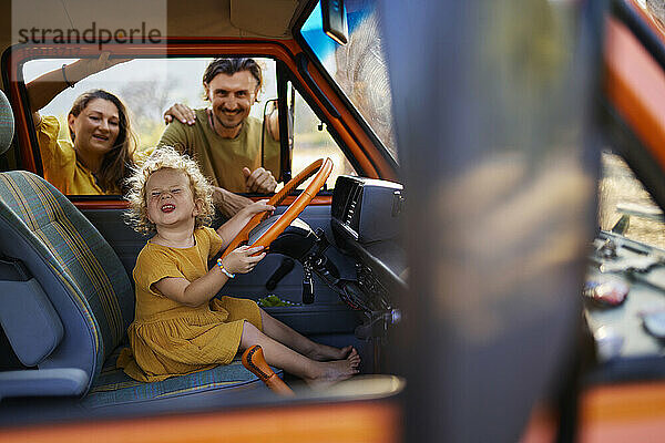 Mädchen spielt mit Lenkrad im Wohnwagen von Mutter und Vater